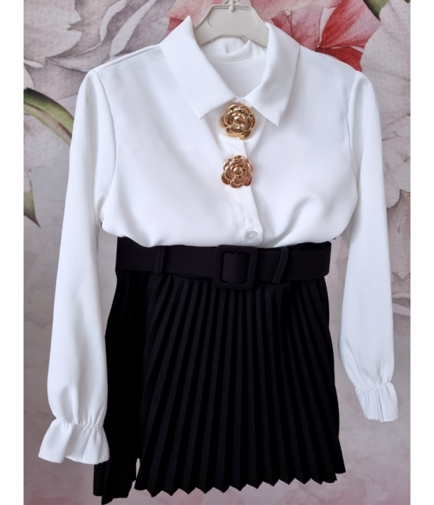 Stylowy zestaw galowy dla dziewczynki składający się z białej koszuli ze złotymi odpinanymi ozdobami oraz czarnej plisowanej spódniczki z paskiem. Idealny jako elegancki strój dla dziewczynki na szkolne uroczystości, akademie, święta i rodzinne okazje.
