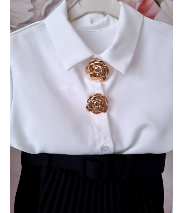 Stylowy zestaw galowy dla dziewczynki składający się z białej koszuli ze złotymi odpinanymi ozdobami oraz czarnej plisowanej spódniczki z paskiem. Idealny jako elegancki strój dla dziewczynki na szkolne uroczystości, akademie, święta i rodzinne okazje.