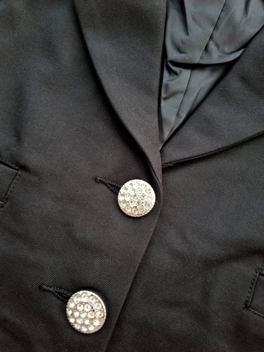 Czarny elegancki garnitur dla dziewczynki z krótką marynarką ozdobioną kryształowymi guzikami i kokardą z tyłu oraz spodniami z wysokim stanem i szeroką nogawką.